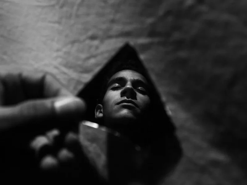 Twarz mężczyzny odbita w odłamku rozbitego lustra w ciemności — metafora rozszczepionego obrazu siebie u ofiary gaslightingu