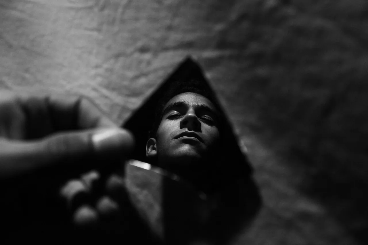 Twarz mężczyzny odbita w odłamku rozbitego lustra w ciemności — metafora rozszczepionego obrazu siebie u ofiary gaslightingu