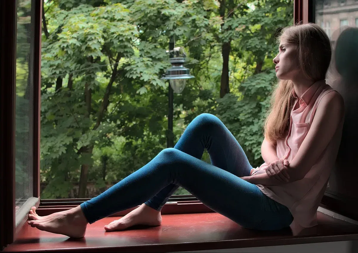 Kobieta siedzi przy oknie, patrzy w zieleń — codzienna uważność bez Instagrama