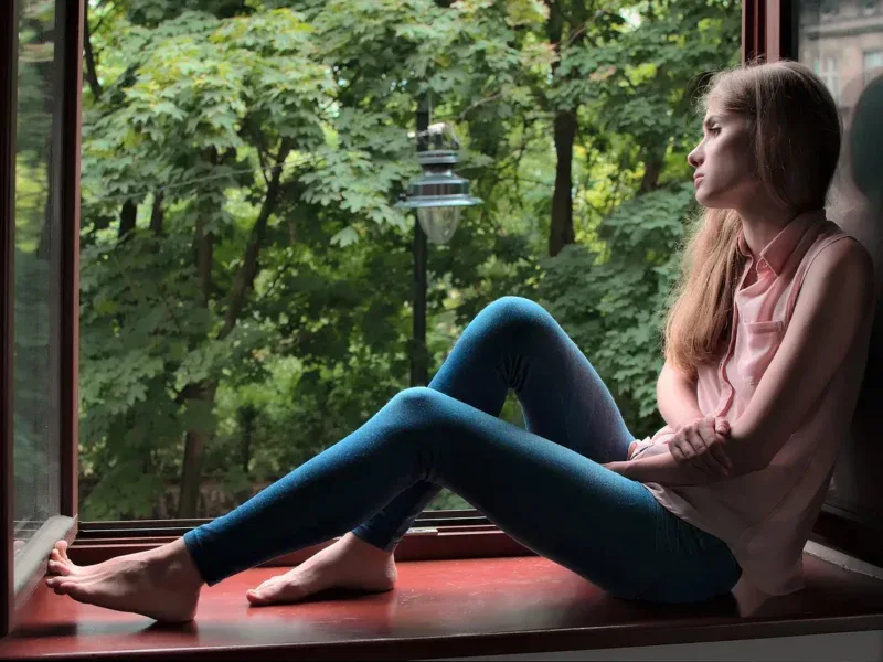 Kobieta siedzi przy oknie, patrzy w zieleń — codzienna uważność bez Instagrama