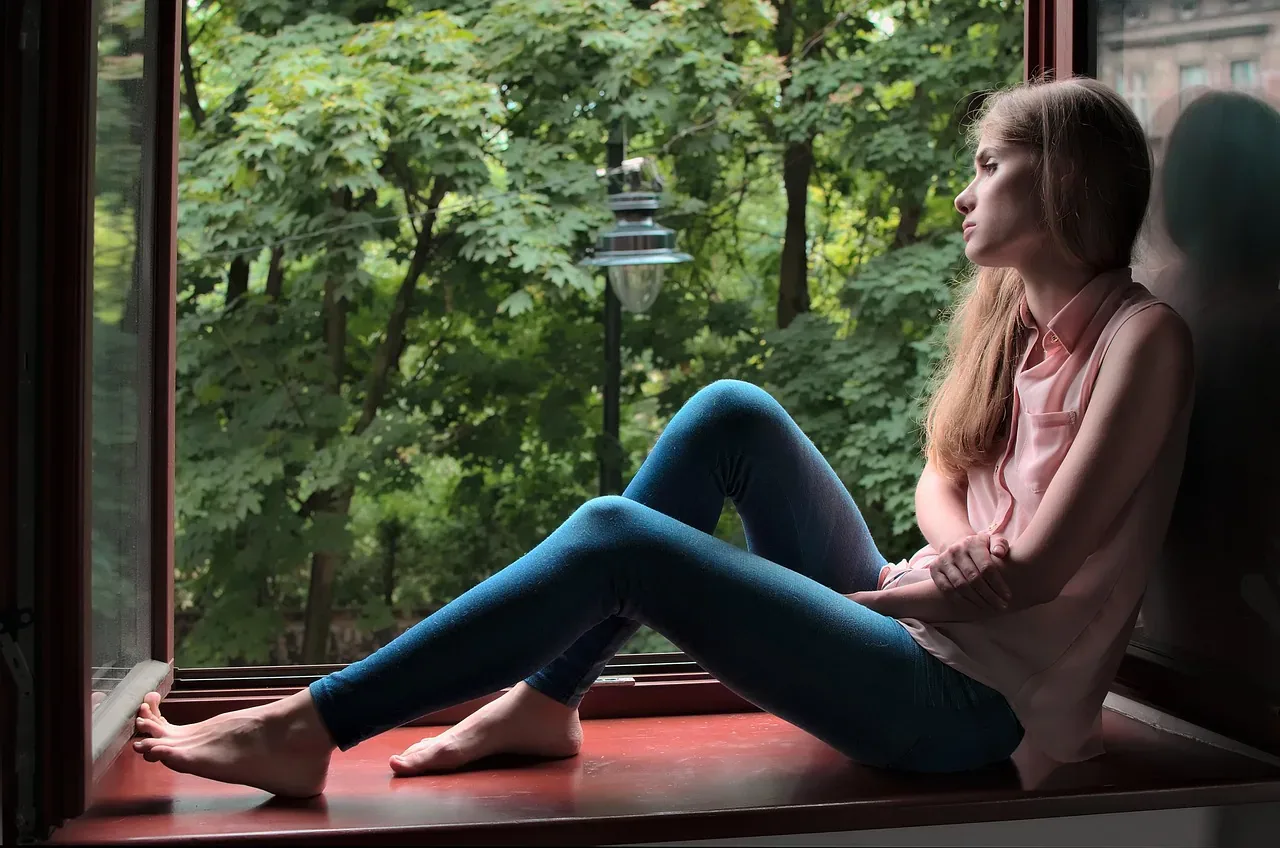 Kobieta siedzi przy oknie, patrzy w zieleń — codzienna uważność bez Instagrama