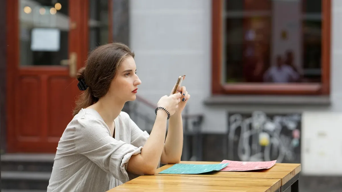 Kobieta w kawiarnianym ogródku patrzy na telefon i czeka na odpowiedź, breadcrumbing w randkowaniu