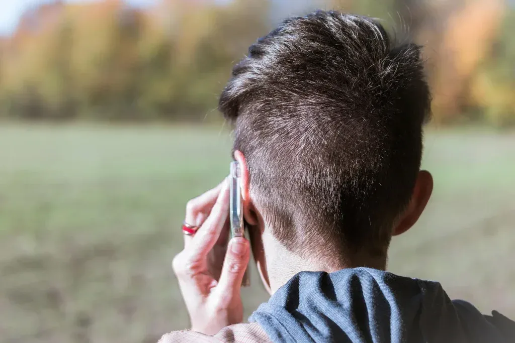 Osoba rozmawia przez telefon na tle pola: rozmowa z telefonem wsparcia jako pierwszy krok po pomoc