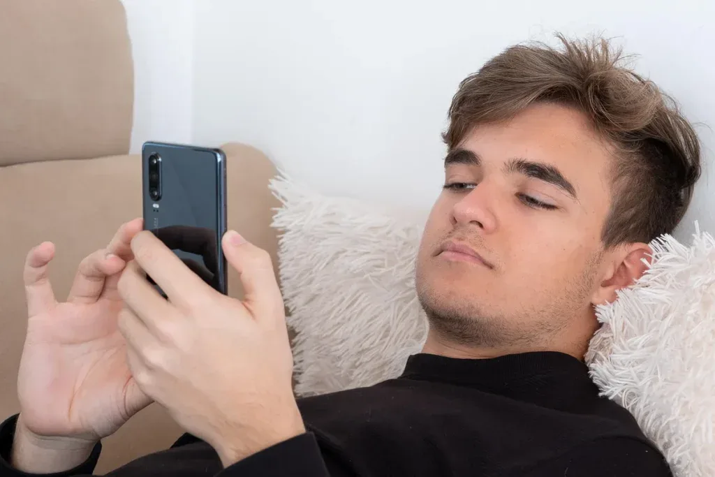 Mężczyzna leży na kanapie i od niechcenia pisze wiadomości w telefonie